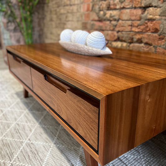 A blackwood coffee table with white ornamental balls atop, on a white rug and set against a brick wall.