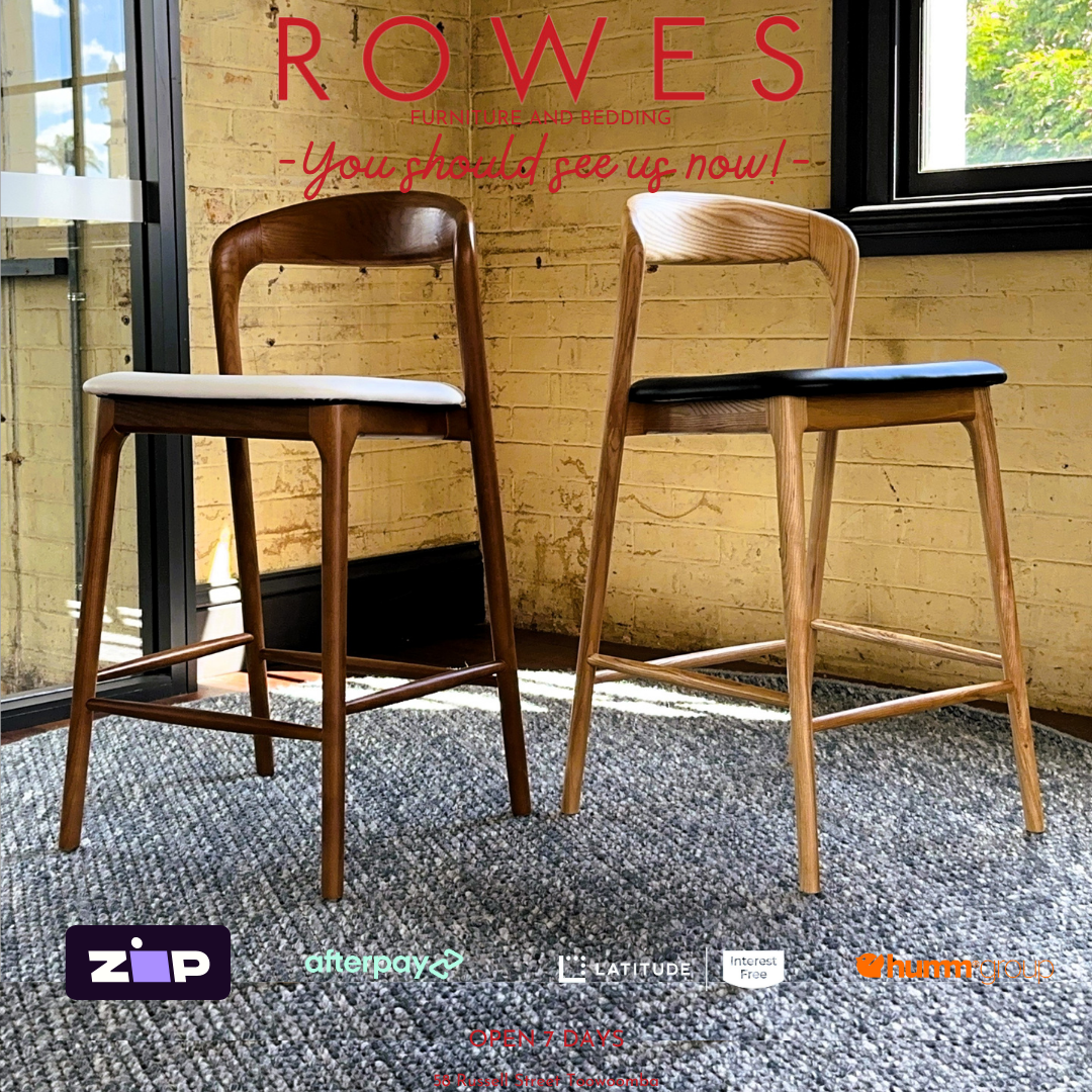 Two wooden bar stools with black seats in a room with a brick wall and large windows.