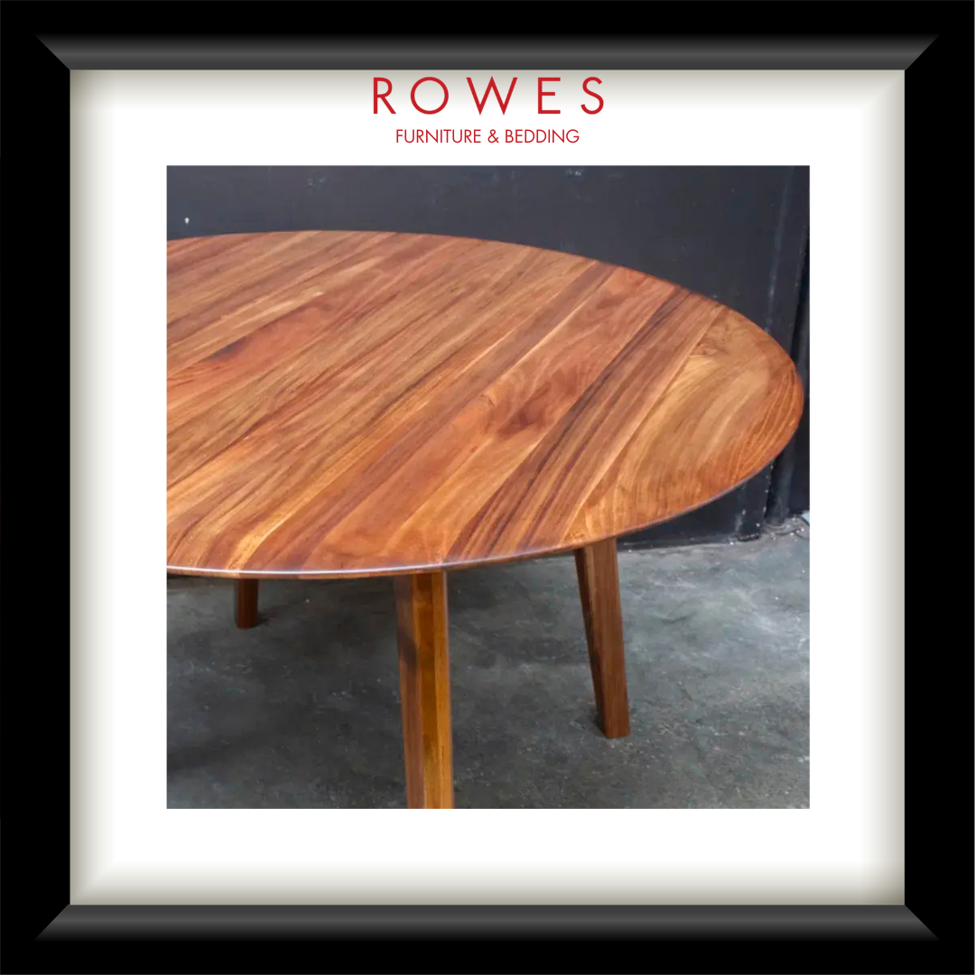 A framed product photo of a round wooden table with a warm medium-brown wood grain finish and tapered legs, presented with a white mat and black frame. The brand name 'ROWES FURNITURE & BEDDING' is printed at the top of the frame.