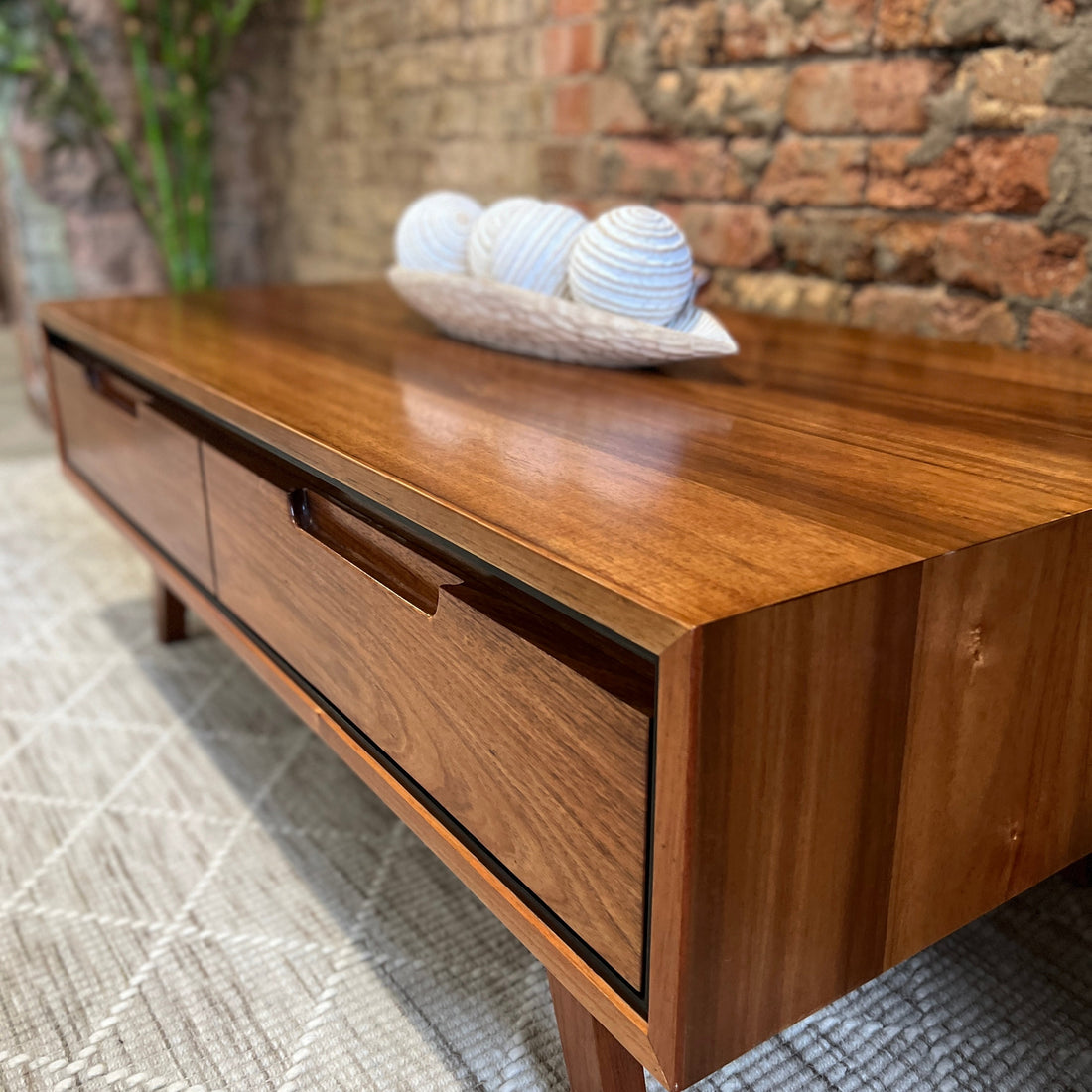 A blackwood coffee table with white ornamental balls atop, on a white rug and set against a brick wall.