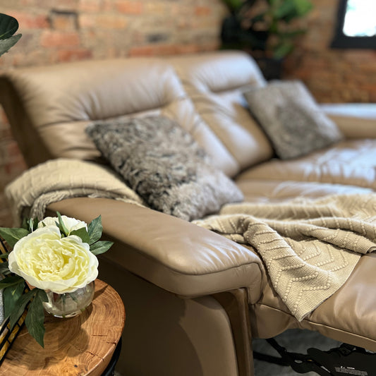 Stressless reclining sofa with cushions and throw, next to a side table and set against a brick wall