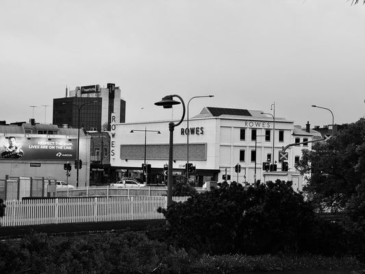 A city landscape in black and white with a large white building featuring ROWES branding on the sides.
