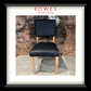 A framed product photograph of a modern dining chair with a black upholstered seat and backrest and light wood legs, set against a brick wall. The photo is matted with a white border and enclosed in a black frame, with the text 'ROWES FURNITURE & BEDDING' printed at the top.