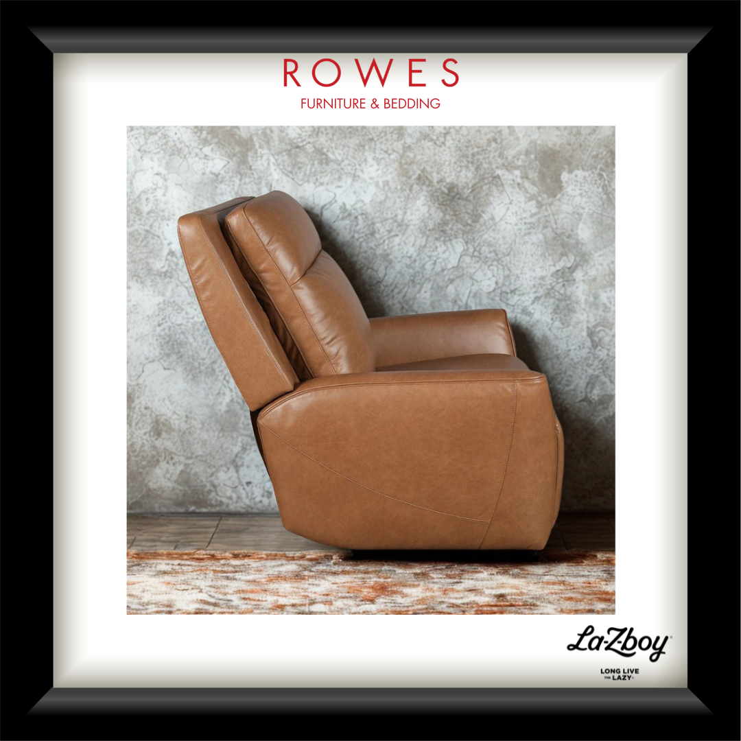 A framed print featuring a tan leather recliner chair against a textured gray wall, with the text 'ROWES FURNITURE & BEDDING' at the top and 'LaZboy' at the bottom. The print is matted with a white border and enclosed in a black frame.