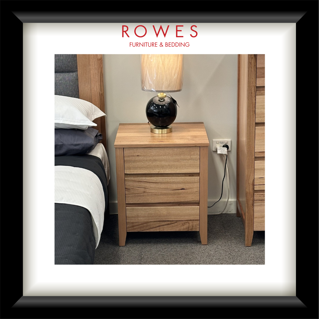 Wooden nightstand with lamp next to bed in a bedroom setting, featuring Rowes Furniture & Bedding logo.