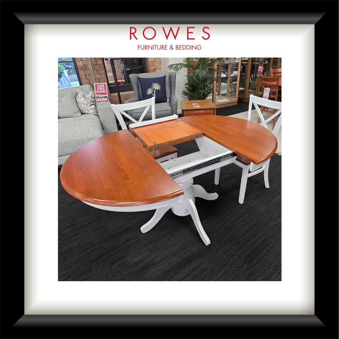 A white dining table surrounded by matching chairs. The top of the dining table and the seats of the chairs are all natural timber coloured. The Rowes branding is prominent. 