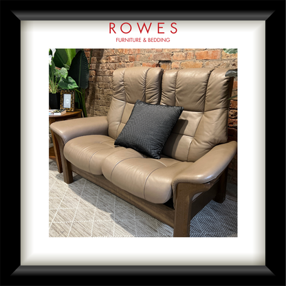 Brown leather sofa with a black pillow in a room with a brick wall and plants, featuring the Rowes Furniture & Bedding logo.