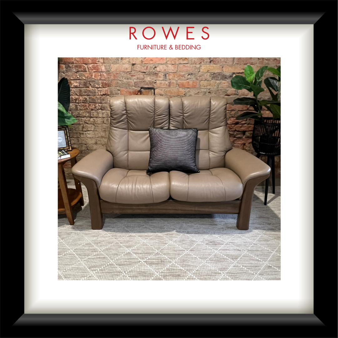 Brown leather sofa with a gray pillow in a room with a brick wall and plants.