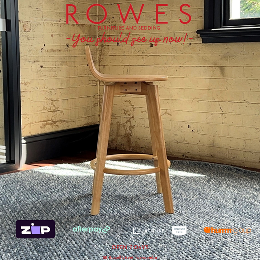 Wooden bar stool in a room with brick walls and a window, featuring the brand 'Rowes'.