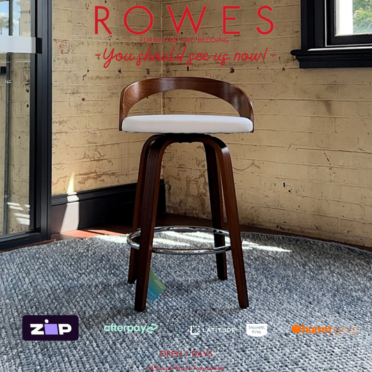 Wooden bar stool with white cushion on a gray carpeted floor against a brick wall, with 'Rowes' branding above.