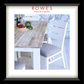 A framed catalog-style interior scene showing a wooden dining table with white chairs, a bottle, grapes, and greenery on a light stone floor, with the text 'ROWES FURNITURE & BEDDING' at the top. The frame is black with a white mat.