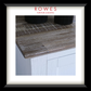 A framed interior photograph showing a rustic weathered wood tabletop corner with white cabinetry below, a white mat, and a black frame. The brand name 'ROWES FURNITURE & BEDDING' appears in red at the top of the frame.