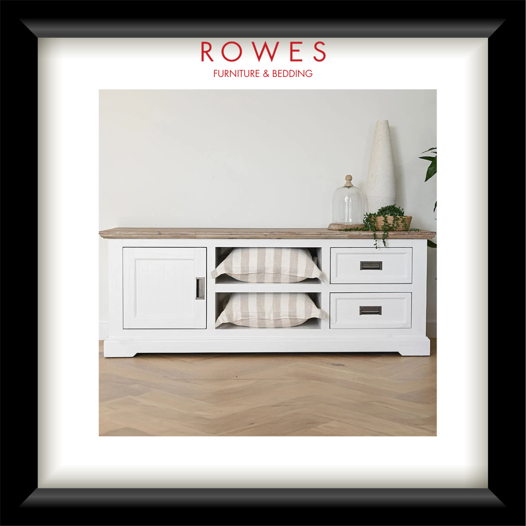 A framed interior photo print featuring a white wooden media console with a light wood top, two open shelves with striped cushions, and two drawers. The print is matted with a wide white border and a thick black frame.