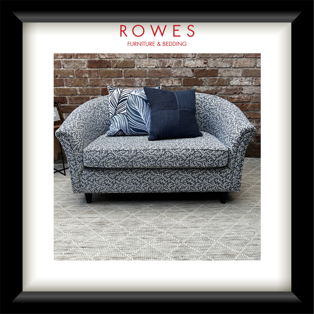 Gray floral-patterned sofa with blue pillows against a brick wall, featuring 'Rowes Furniture & Bedding' logo.