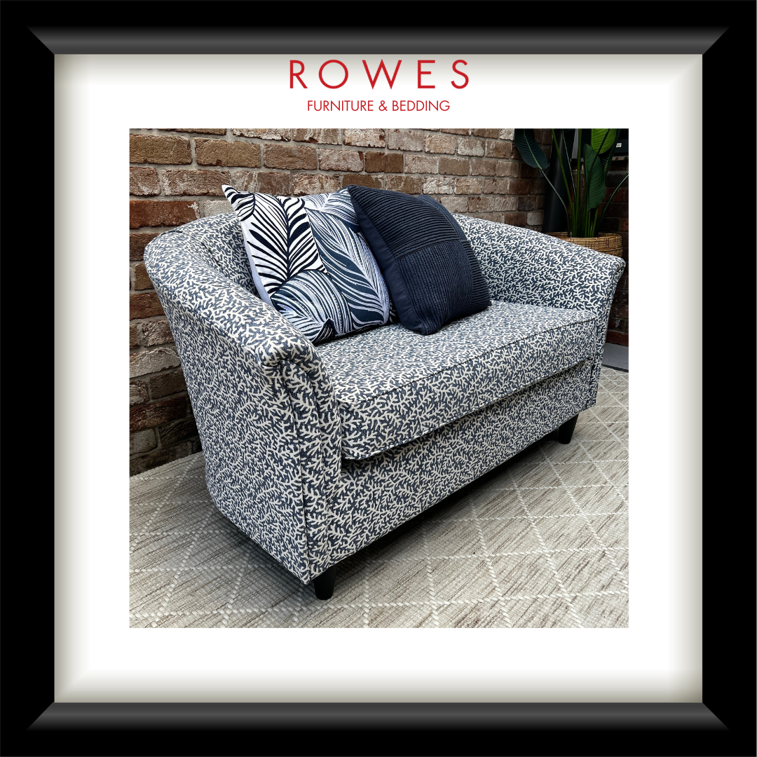 Patterned sofa with decorative pillows against a brick wall, featuring the Rowes Furniture & Bedding logo.