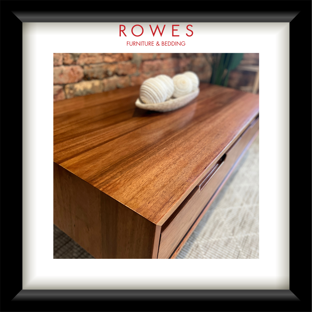 A framed interior design print featuring a warm brown wooden table with a woven bowl of white balls, under the brand name ROWES FURNITURE & BEDDING.