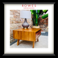 A framed product photo of a mid-century modern wooden side table with a drawer, styled with a table lamp on top. The image is presented with a white mat and a thick black frame, with the brand name 'ROWES FURNITURE & BEDDING' printed at the top.