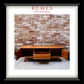 A framed print or poster featuring a mid-century wooden media console in front of a brick wall, with the text 'ROWES FURNITURE & BEDDING' at the top. The artwork is presented in a white mat and a thick black frame.