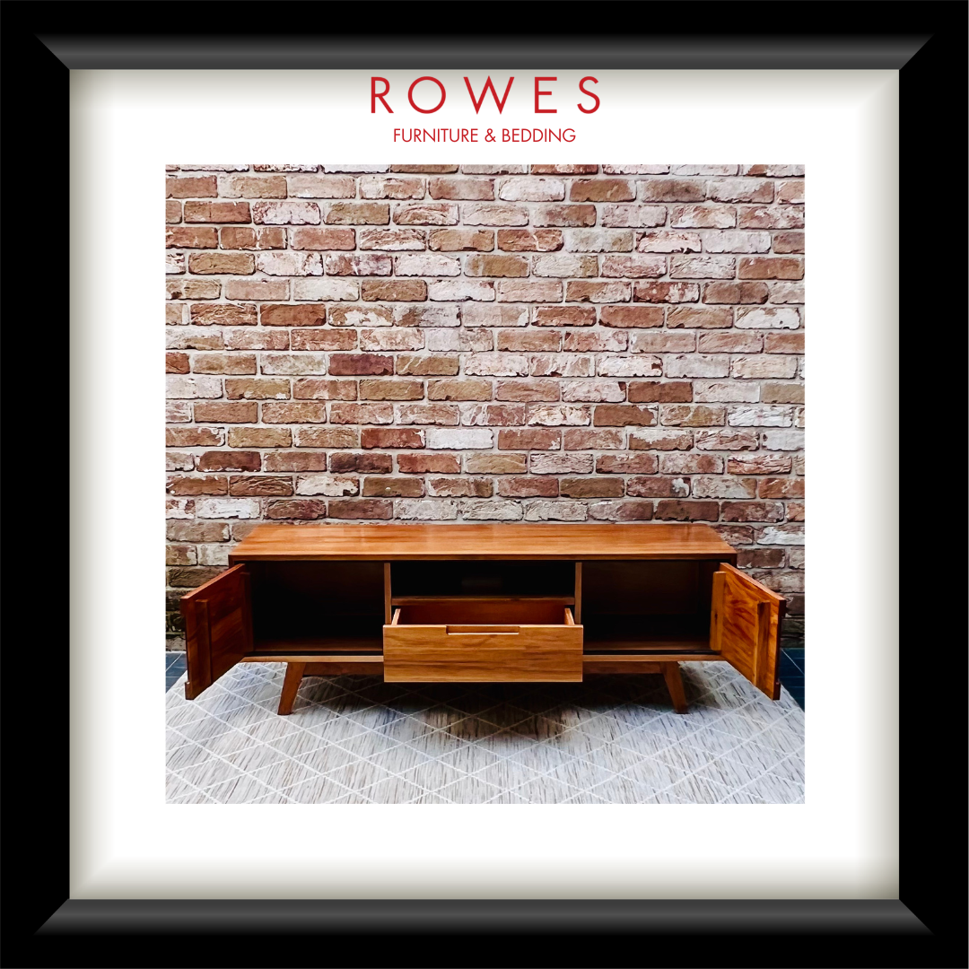 A framed print or poster featuring a mid-century wooden media console in front of a brick wall, with the text 'ROWES FURNITURE & BEDDING' at the top. The artwork is presented in a white mat and a thick black frame.