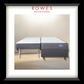 A framed product photograph of a Rowes double mattress setup, featuring a gray upholstered base and two mattresses on a white and light wood floor, set against a beige wall. The image is presented in a black frame with a white mat and the brand name 'ROWES FURNITURE & BEDDING' printed at the top.