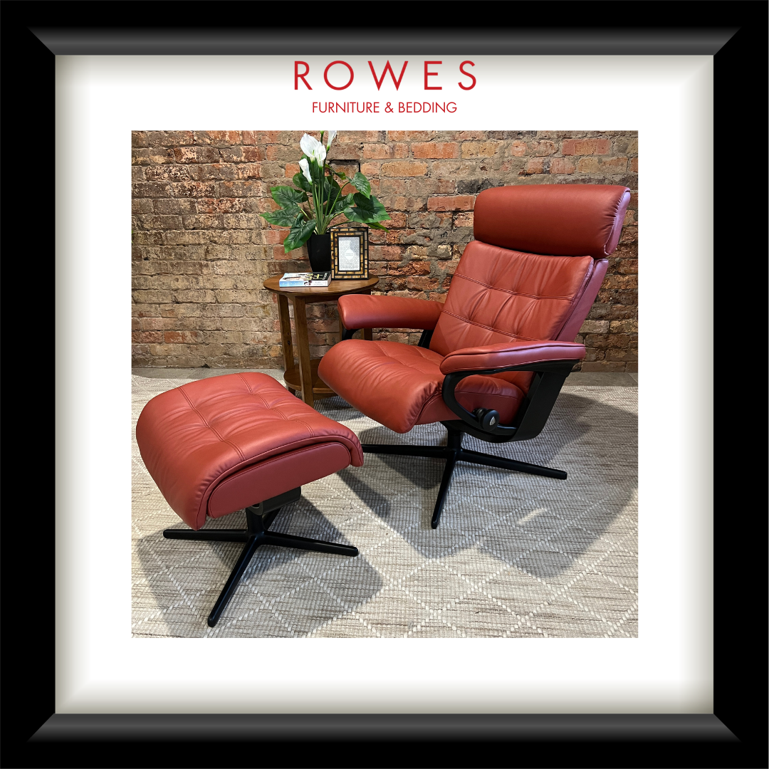 Red leather armchair and ottoman with a small table and plant against a brick wall, branded 'Rowes Furniture & Bedding'.