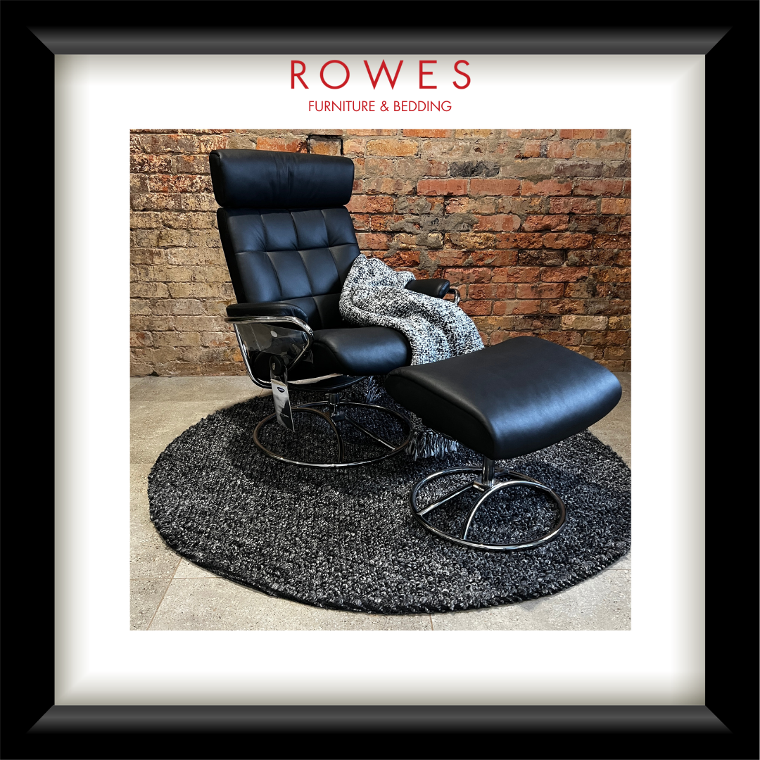 Black leather recliner chair with ottoman on a textured rug against a brick wall, branded 'Rowes'.