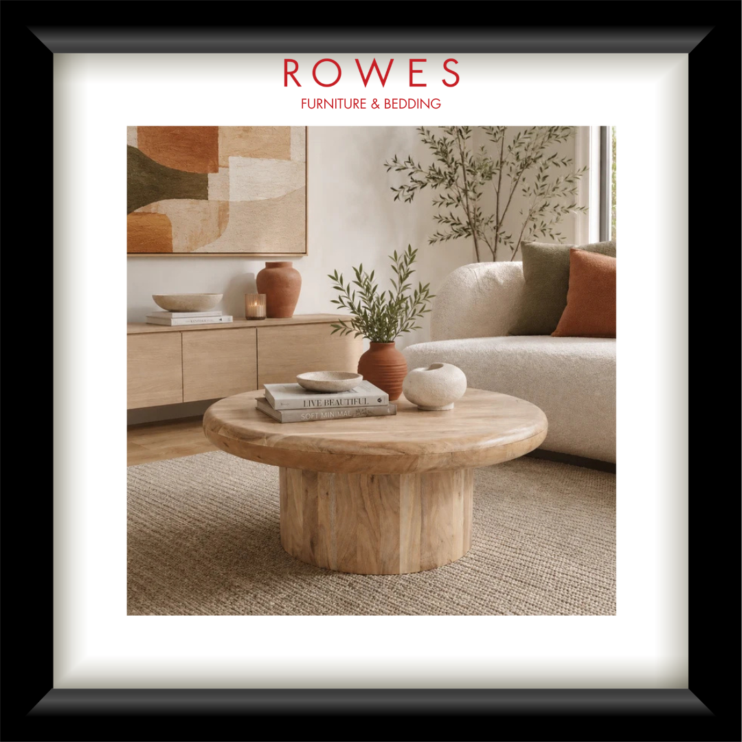 A framed interior design print from Rowes Furniture & Bedding, showcasing a modern living room scene with a round natural wood coffee table, textured beige sofa, and warm neutral decor.