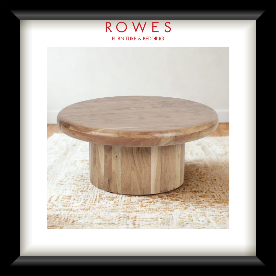 A framed catalog-style photograph of a round wooden coffee table on a textured rug, with the ROWES FURNITURE & BEDDING logo printed at the top. The frame is black with a white mat.