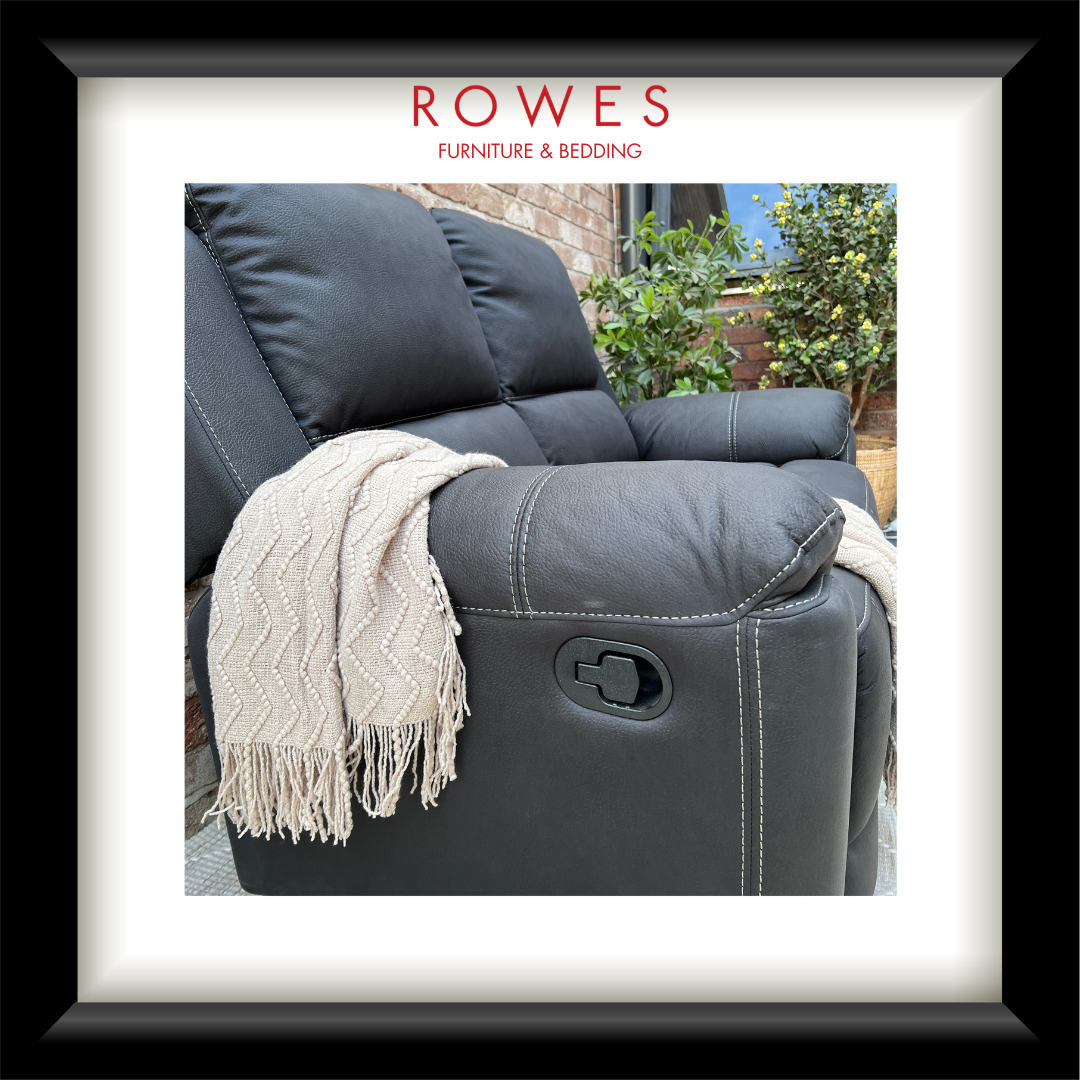A framed product photograph of a dark gray upholstered recliner chair with a cream throw blanket draped over the arm. The photo is presented within a white mat and a black frame, with the brand name 'ROWES FURNITURE & BEDDING' printed at the top.