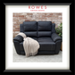 A black leather reclining loveseat shown inside a framed print or matted photo, with a brick wall background and a cream throw blanket draped over one arm. The brand name ROWES FURNITURE & BEDDING appears at the top of the framed presentation.