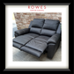 A black leather reclining loveseat sofa shown in a showroom setting with a brick wall background, framed by a white mat and a black frame. The brand name 'ROWES FURNITURE & BEDDING' is printed at the top of the image.