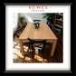 A framed furniture catalog photo showing a light oak dining table with black chairs, presented in a white mat and black frame. The top of the print features the text 'ROWES FURNITURE & BEDDING'.