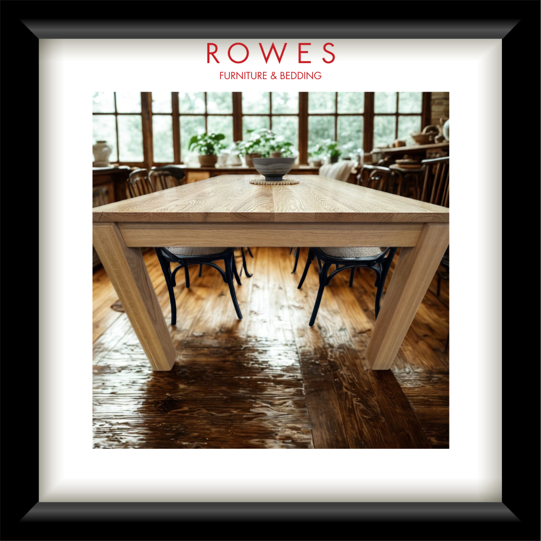 A framed furniture catalog photo showing a light oak dining table with black chairs, presented in a white mat and black frame. The top of the print features the text 'ROWES FURNITURE & BEDDING'.