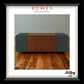 A framed product photograph of a modern rectangular ottoman or coffee table with a dark wood center panel and dark gray fabric side panels, set on a wood floor against a light gray wall. The frame has a white mat and a black frame, with the brand name 'ROWES FURNITURE & BEDDING' at the top and 'LaZboy' at the bottom right.