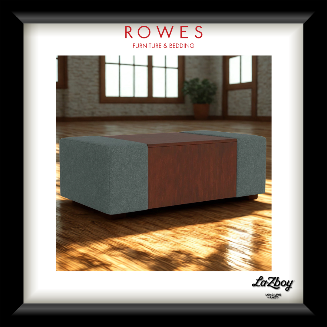 A framed promotional image for a ROWES furniture and bedding product, showing a rectangular ottoman or coffee table with gray fabric sides and a reddish-brown wood center panel, placed in a sunlit room. The frame includes the text 'ROWES FURNITURE & BEDDING' at the top and a 'LaZboy' mark at the bottom right.