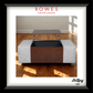 A framed product display showing a Rowes furniture and bedding ottoman with a lift-up coffee table top. The ottoman has light gray textured fabric sides and a dark brown wood-grain front panel.