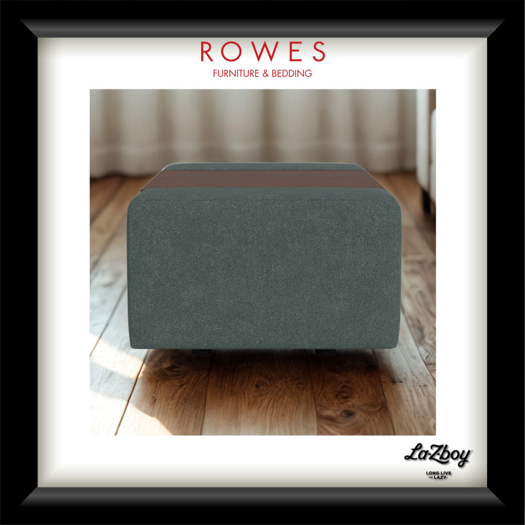 A framed product image of a modern rectangular ottoman in a textured slate gray fabric with a contrasting brown top band, presented on a white mat with a black frame. The top of the frame features the text 'ROWES FURNITURE & BEDDING' in red, and the bottom right corner features the 'LaZboy' brand logo.