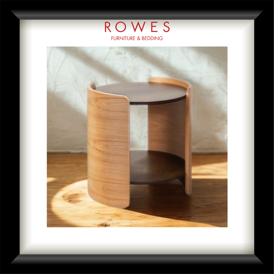 A framed product photograph of a modern wooden side table with curved light-wood panels and dark circular tabletop and lower shelf. The photo is presented inside a white mat and black frame, with the text 'ROWES FURNITURE & BEDDING' at the top.