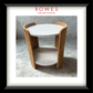 A framed product photograph of a modern round side table with a white top and shelf, supported by curved light oak wood legs, presented with a white mat and black frame. The brand name 'ROWES FURNITURE & BEDDING' is printed at the top of the photo.