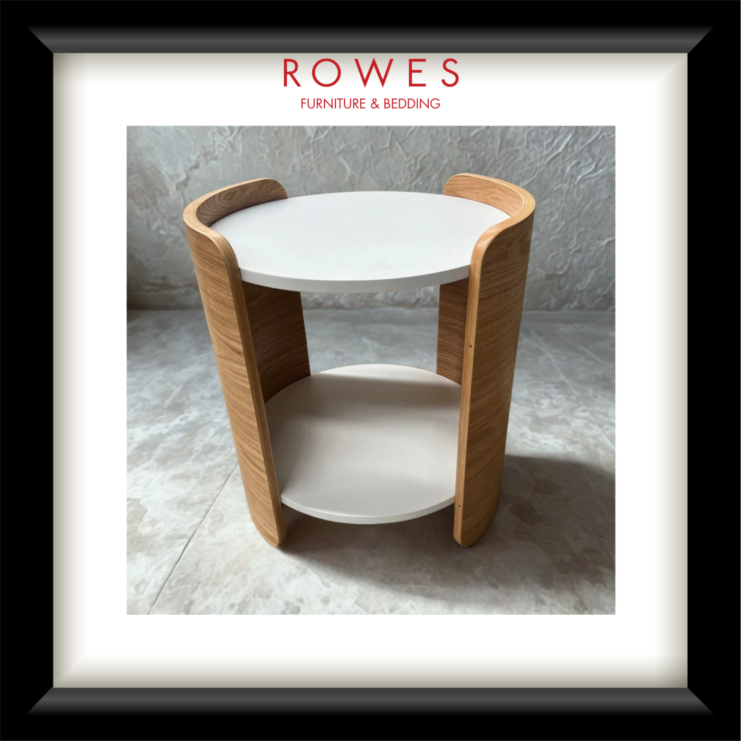 A framed product photograph of a modern round side table with a white top and shelf, supported by curved light oak wood legs, presented with a white mat and black frame. The brand name 'ROWES FURNITURE & BEDDING' is printed at the top of the photo.