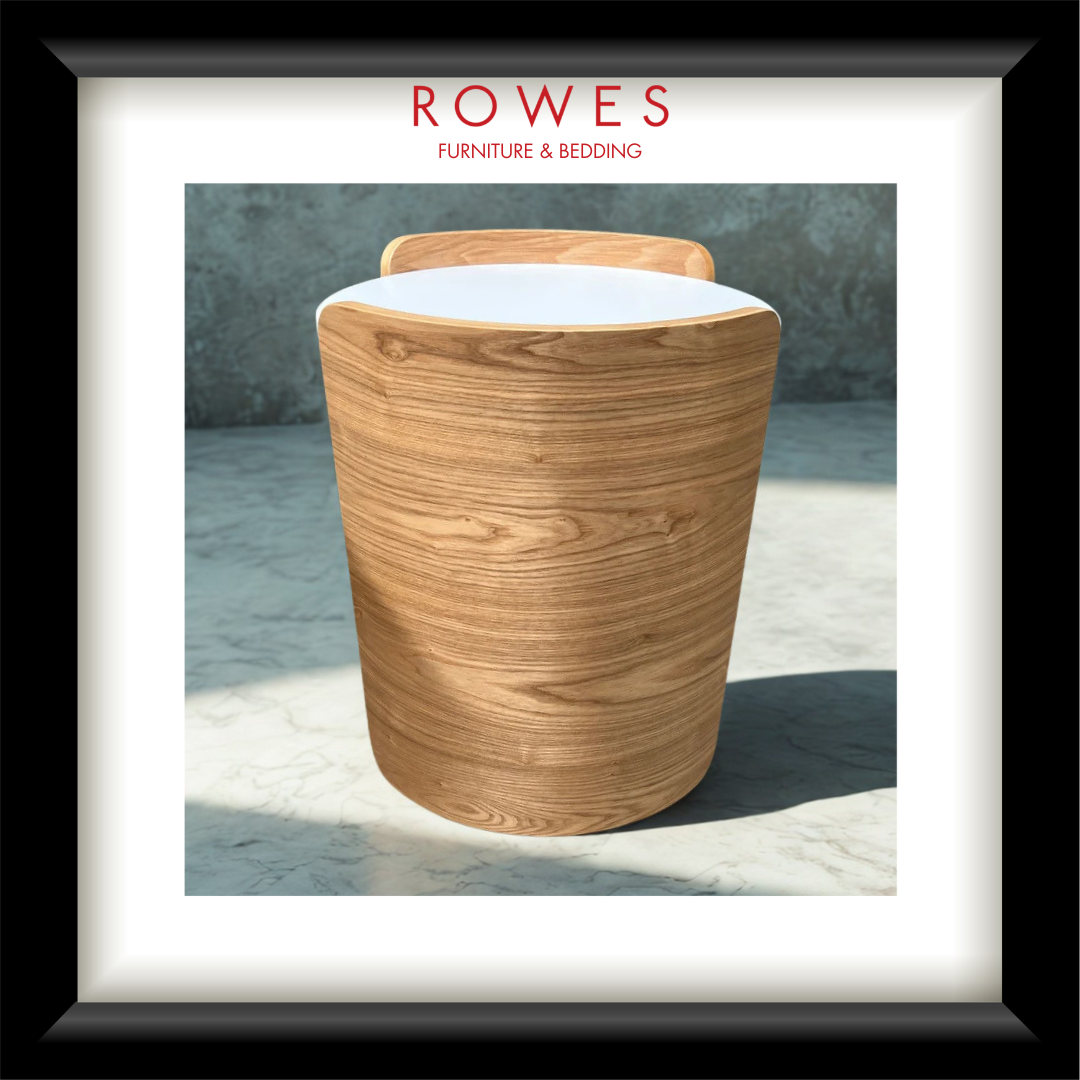 A framed product photograph of a modern cylindrical side table or stool with a light oak wood grain finish and a white top surface, presented with a white mat and black frame. The brand name 'ROWES FURNITURE & BEDDING' is printed at the top of the print.