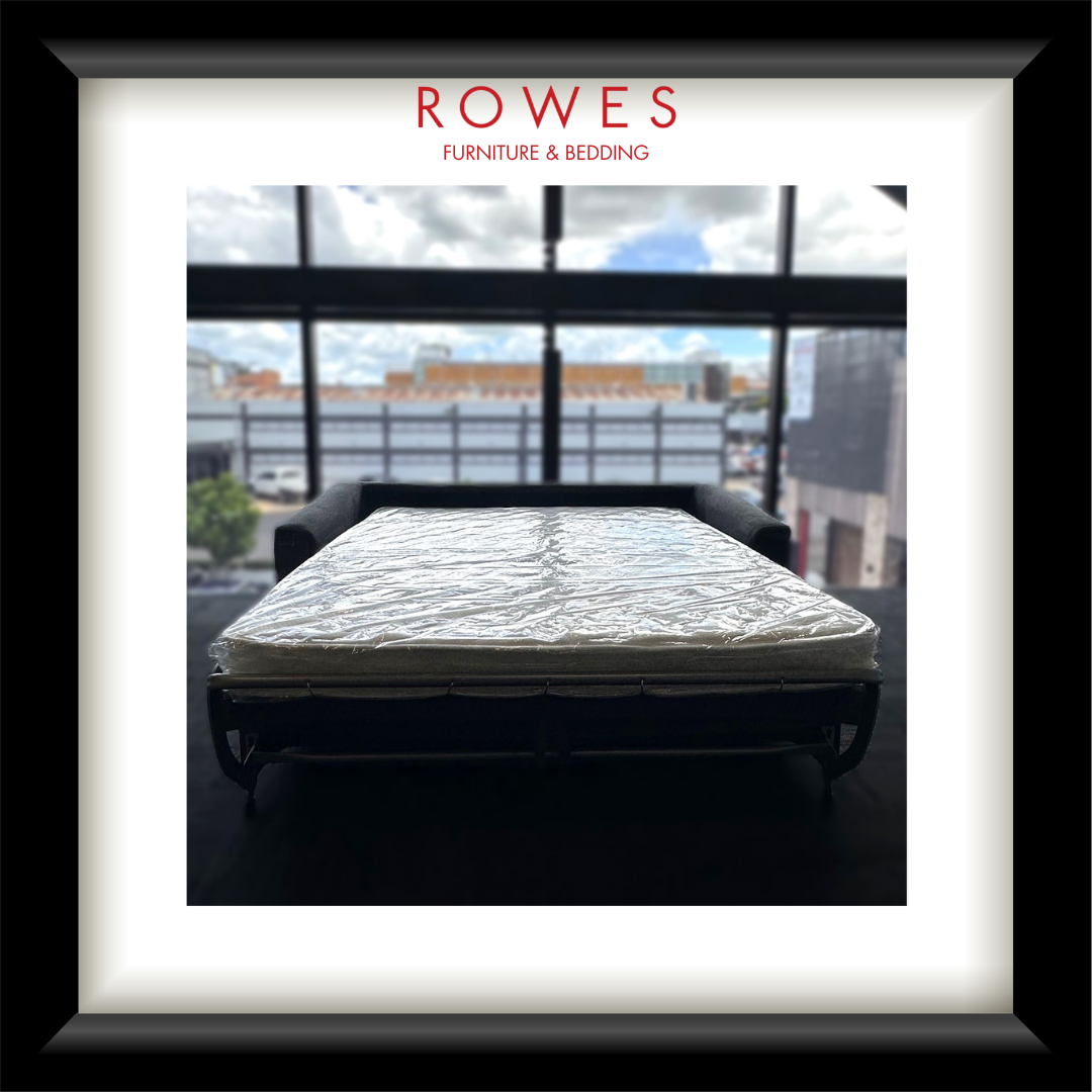 Mattress on a stand with a cityscape view through large windows, branded 'Rowes Furniture & Bedding'.