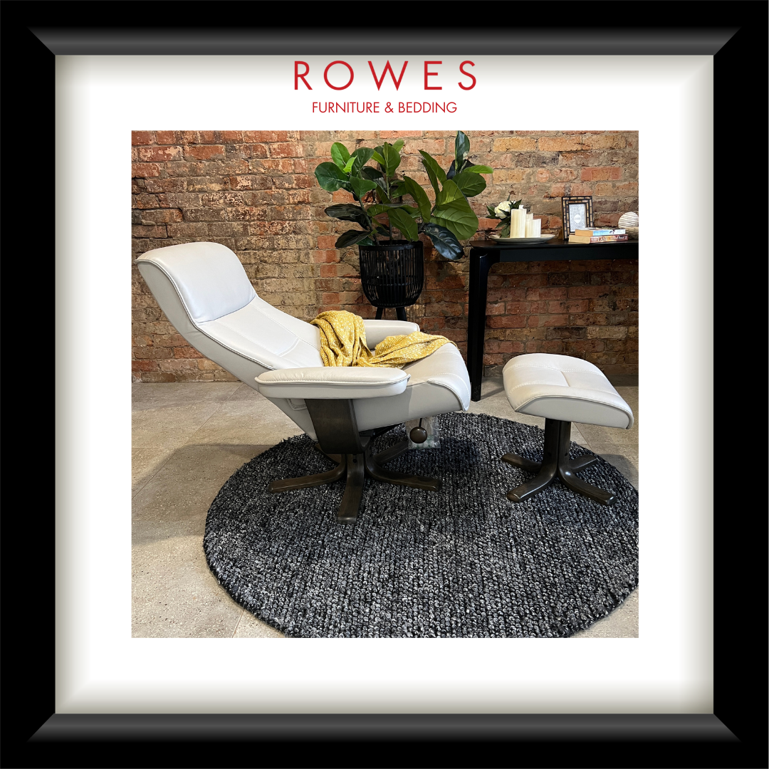 Modern white chair with ottoman on a textured rug in front of a brick wall, with 'Rowes Furniture & Bedding' branding.