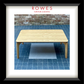 A framed product image of a light natural wood low coffee table on a blue tiled floor against a brick wall, with the brand name 'ROWES FURNITURE & BEDDING' printed at the top. The entire image is enclosed in a white mat and a thick black frame.