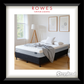 Bed with gray bedding in a room with a lamp and window, featuring 'Rowes Furniture & Bedding' and 'Sleepyhead'.