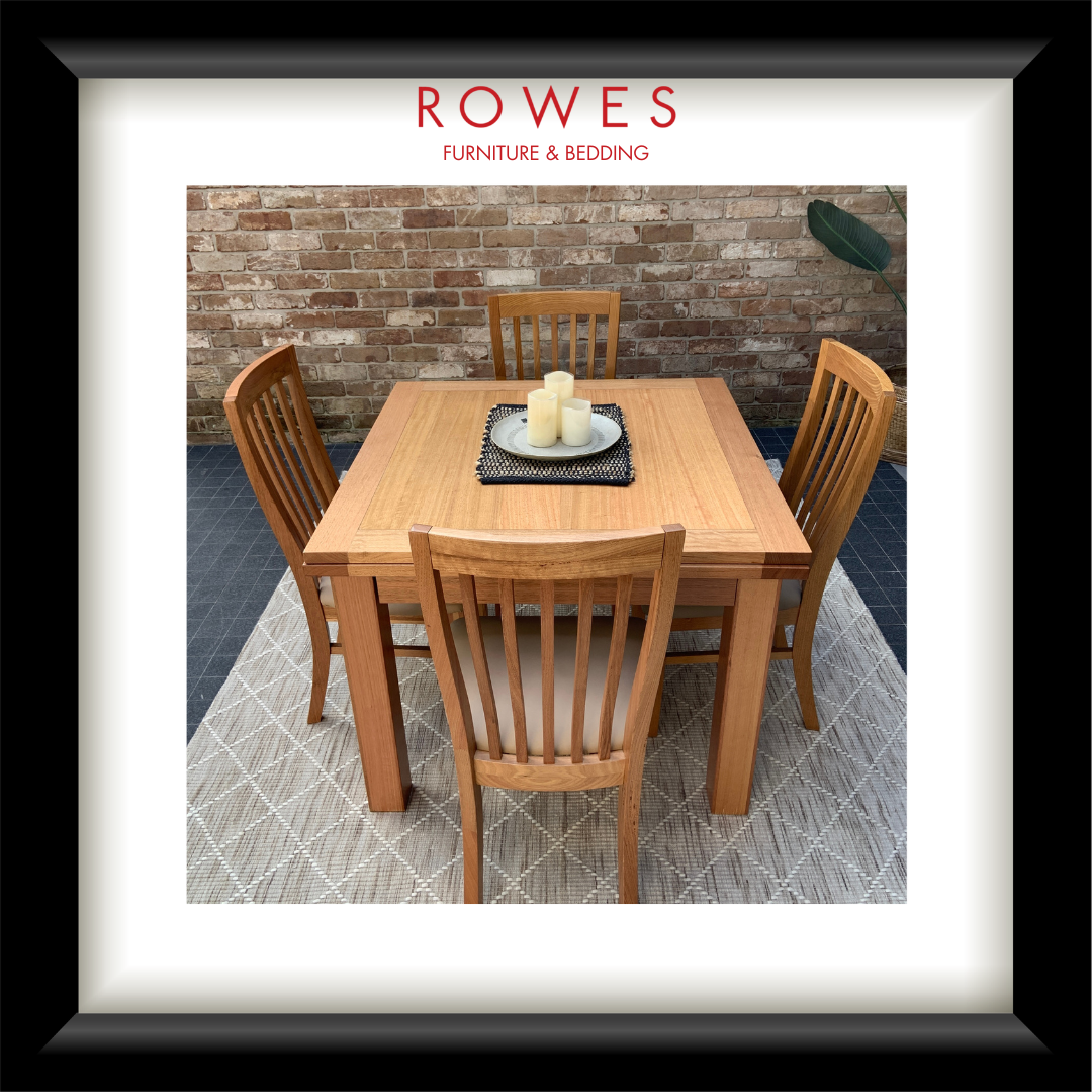 A framed product display featuring a wooden dining table and four matching slat-back chairs on a patterned rug, with a brick wall background. The image is presented inside a white mat and a thick black frame, with the brand name 'ROWES FURNITURE & BEDDING' printed at the top of the photo.