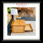 A framed product photo of a wooden side table or nightstand with one drawer pulled open, shown on a patio with a white lamp on top. The image is matted with a white border and a black frame, with the text 'ROWES FURNITURE & BEDDING' at the top.