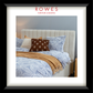 A bedroom scene featuring a large, plush bed with a fabric bedhead and sides, bedsides and a large rug. The Rowes Furniture logo features.
