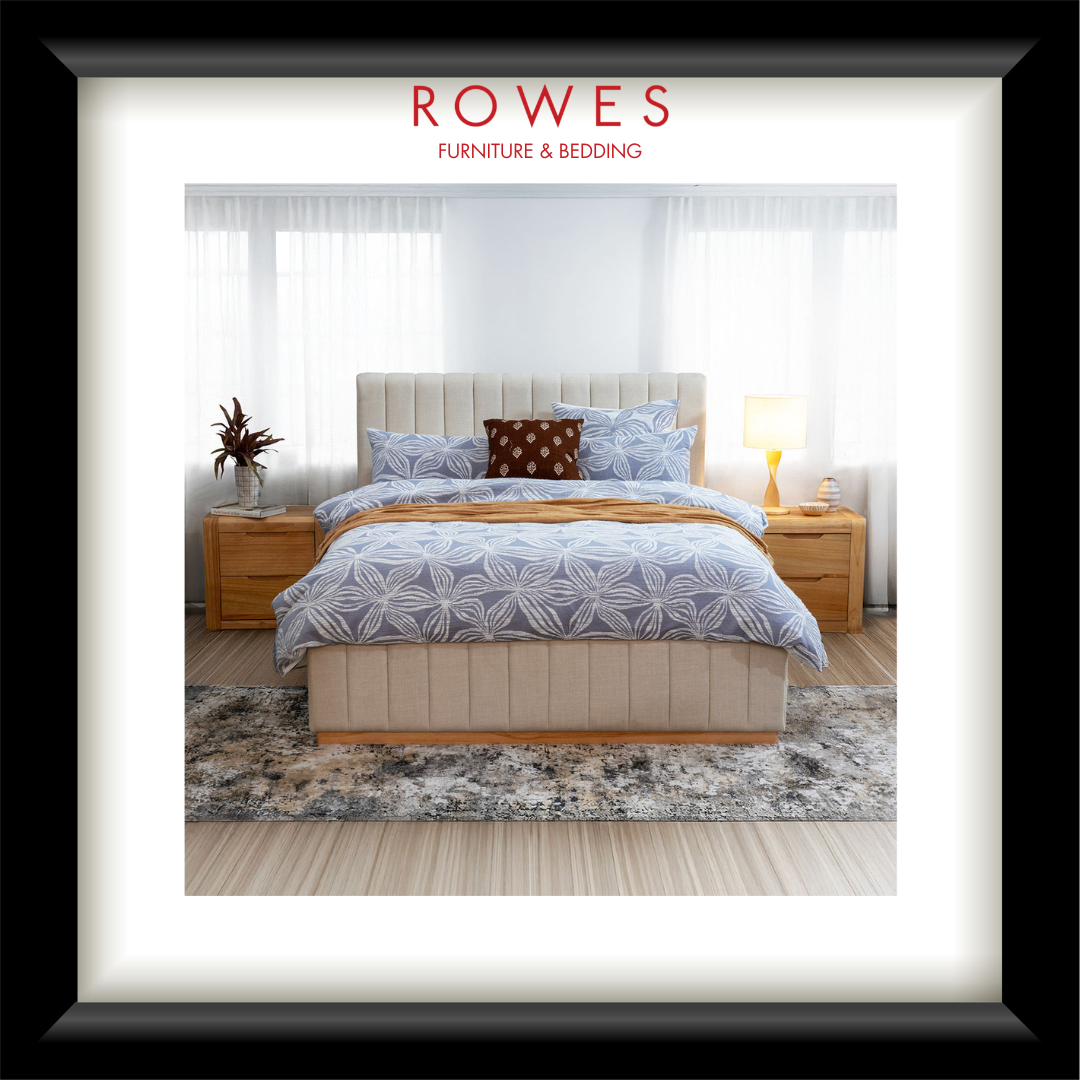 A bedroom scene featuring a large, plush bed with a fabric bedhead and foot, bedsides and a large rug. The Rowes Furniture logo features.