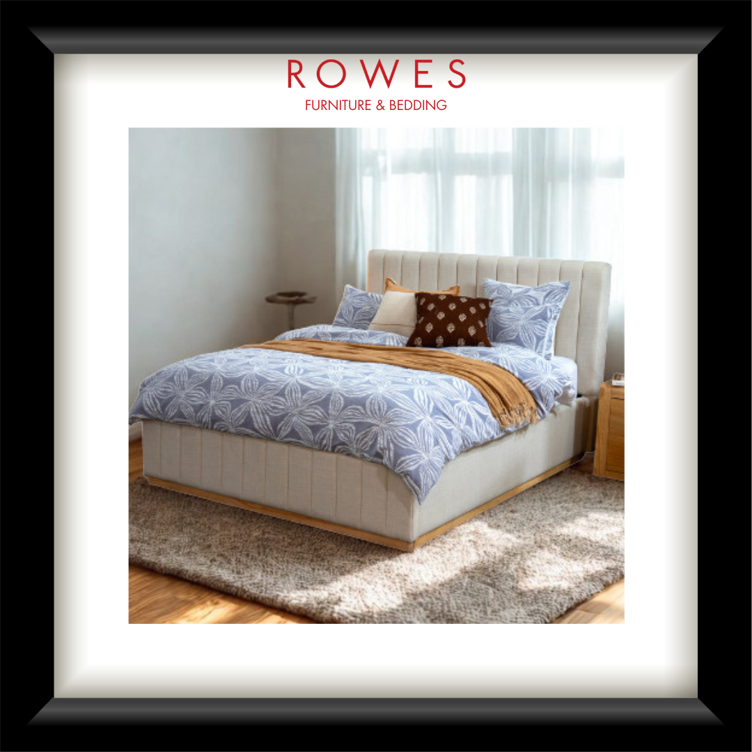 A bedroom scene featuring a large, plush bed with a fabric bedhead and foot, bedsides and a large rug. The Rowes Furniture logo features.